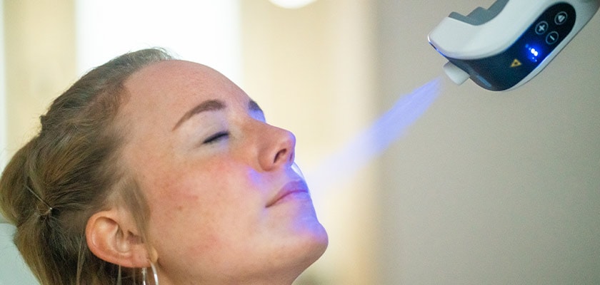 Frau mit entspanntem Gesicht erhält blaue Lichtbehandlung; Fokus auf Gerät.