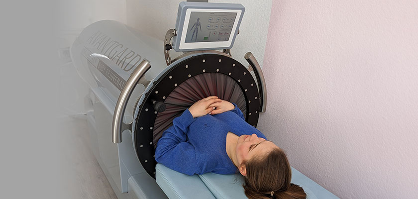 Person in blauem Pullover liegt entspannt in moderner medizinischer Gerätelandschaft.