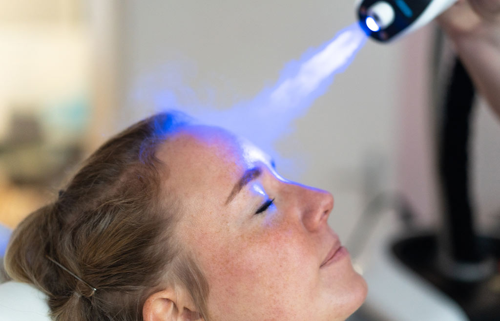 Frau mit entspanntem Gesicht erhält blaue Lichttherapie auf der Stirn.