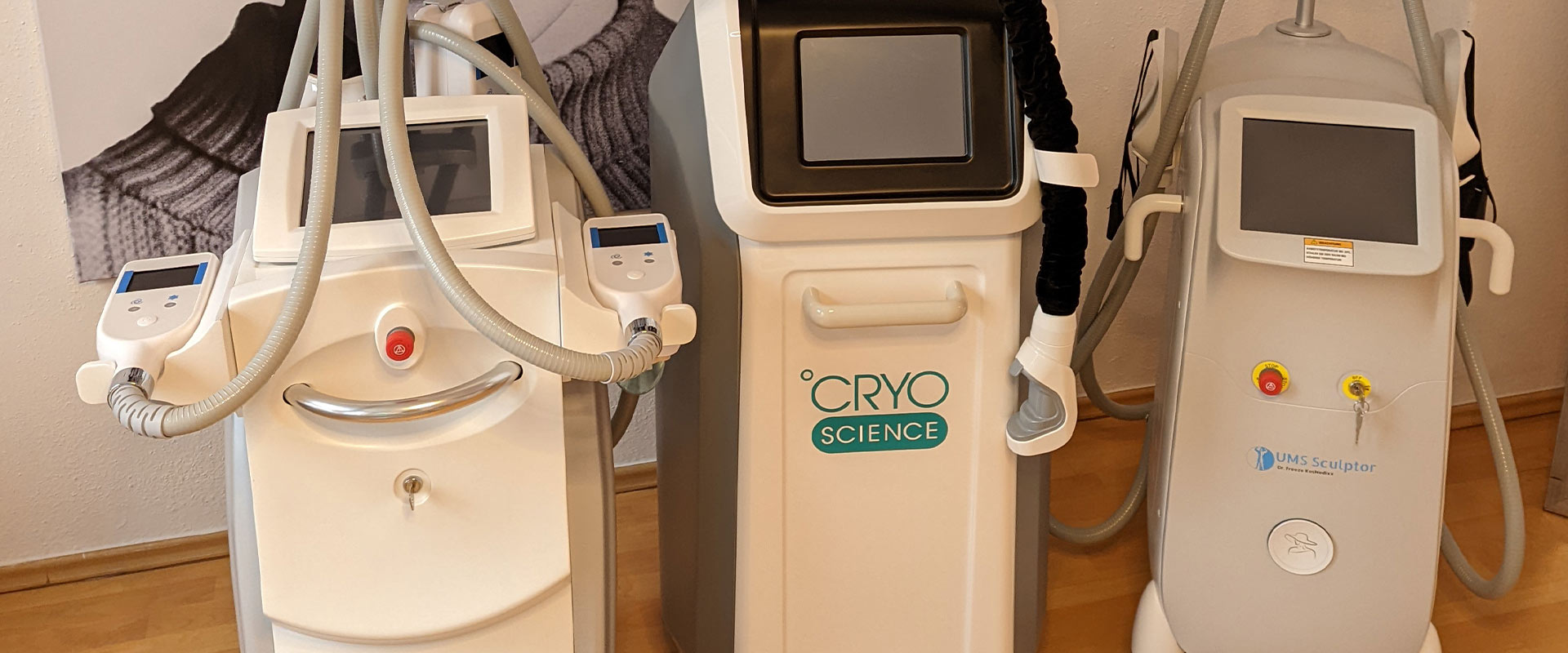 Drei moderne Kryotherapie-Geräte in Weiß mit Anzeigen und Schläuchen auf Holzfußboden.